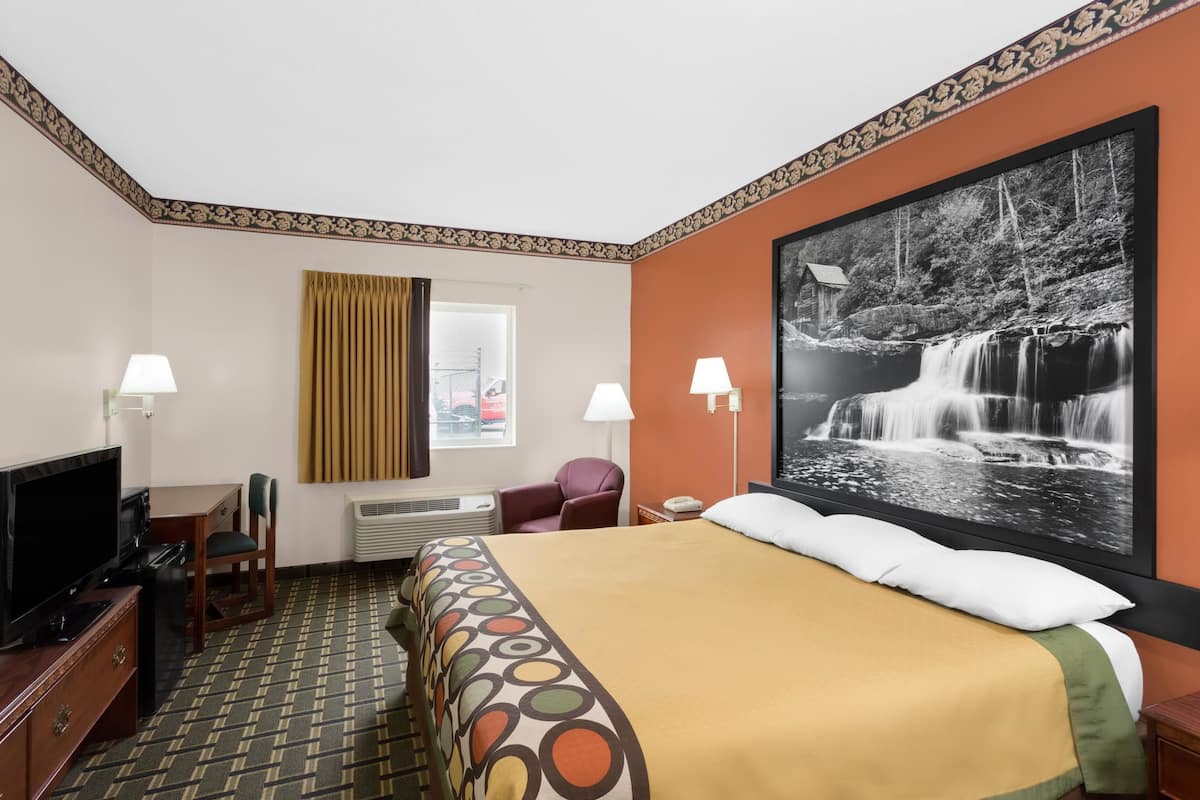 A hotel room with a bed, a TV, a desk, a chair, and a window with curtains.