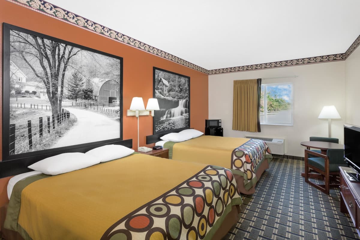 A hotel room with two beds, a TV, a desk, and a window with curtains.