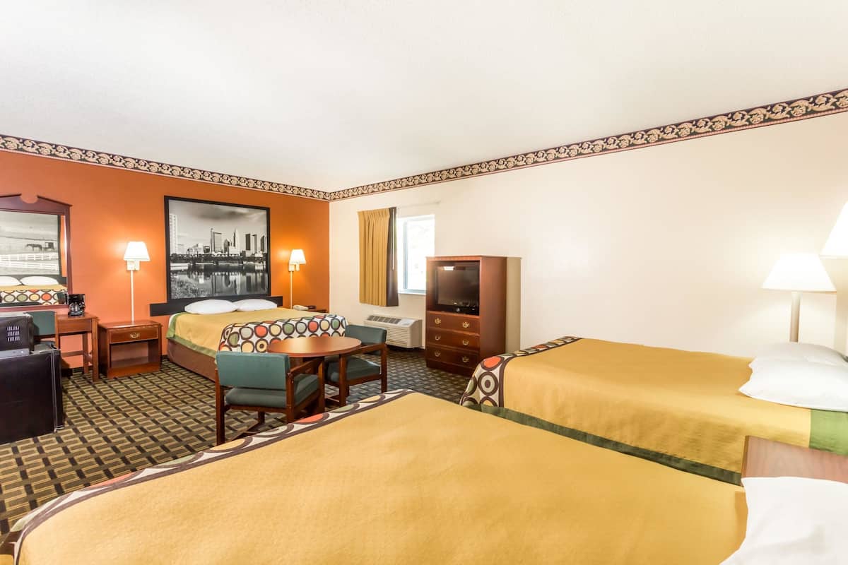 A hotel room with two beds, a desk, a chair, a TV, and a window.
