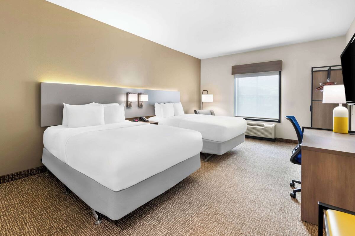 A hotel room with two beds, a desk, a chair, a lamp, and a large window.