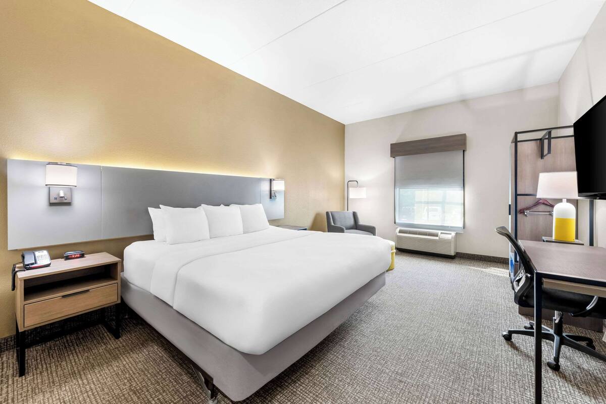 A hotel room with a large bed, bedside tables, a desk, a chair, and a TV.