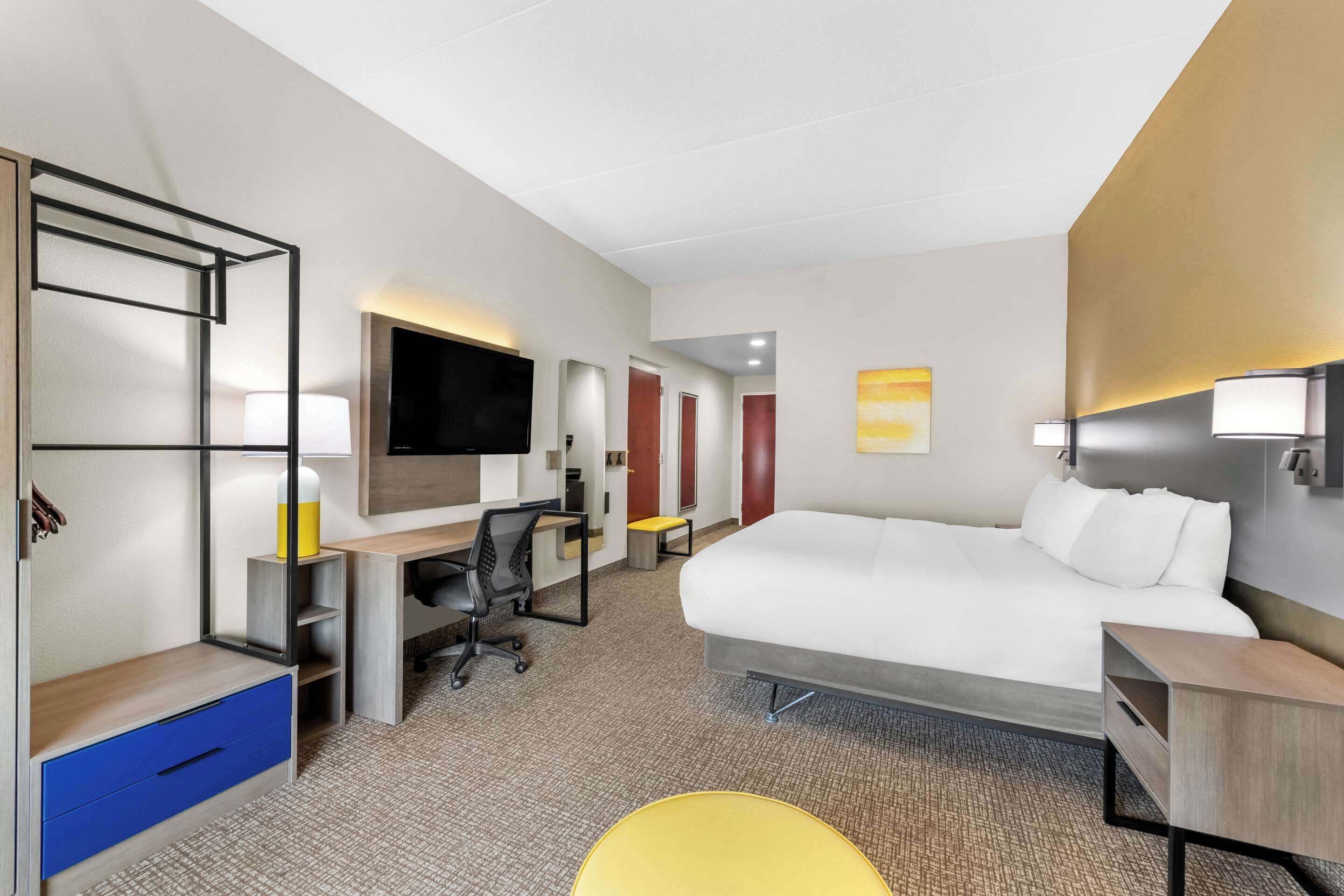 Et moderne hotelværelse med en stor seng, et skrivebord med stol, et fjernsyn og et lille siddeområde.