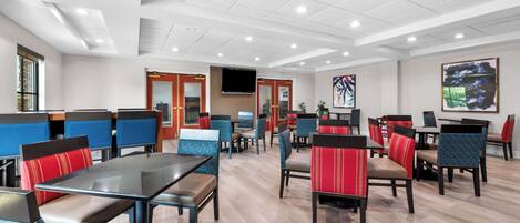 A spacious dining area with multiple tables and chairs, a flat-screen TV mounted on the wall, and a large painting on the wall.