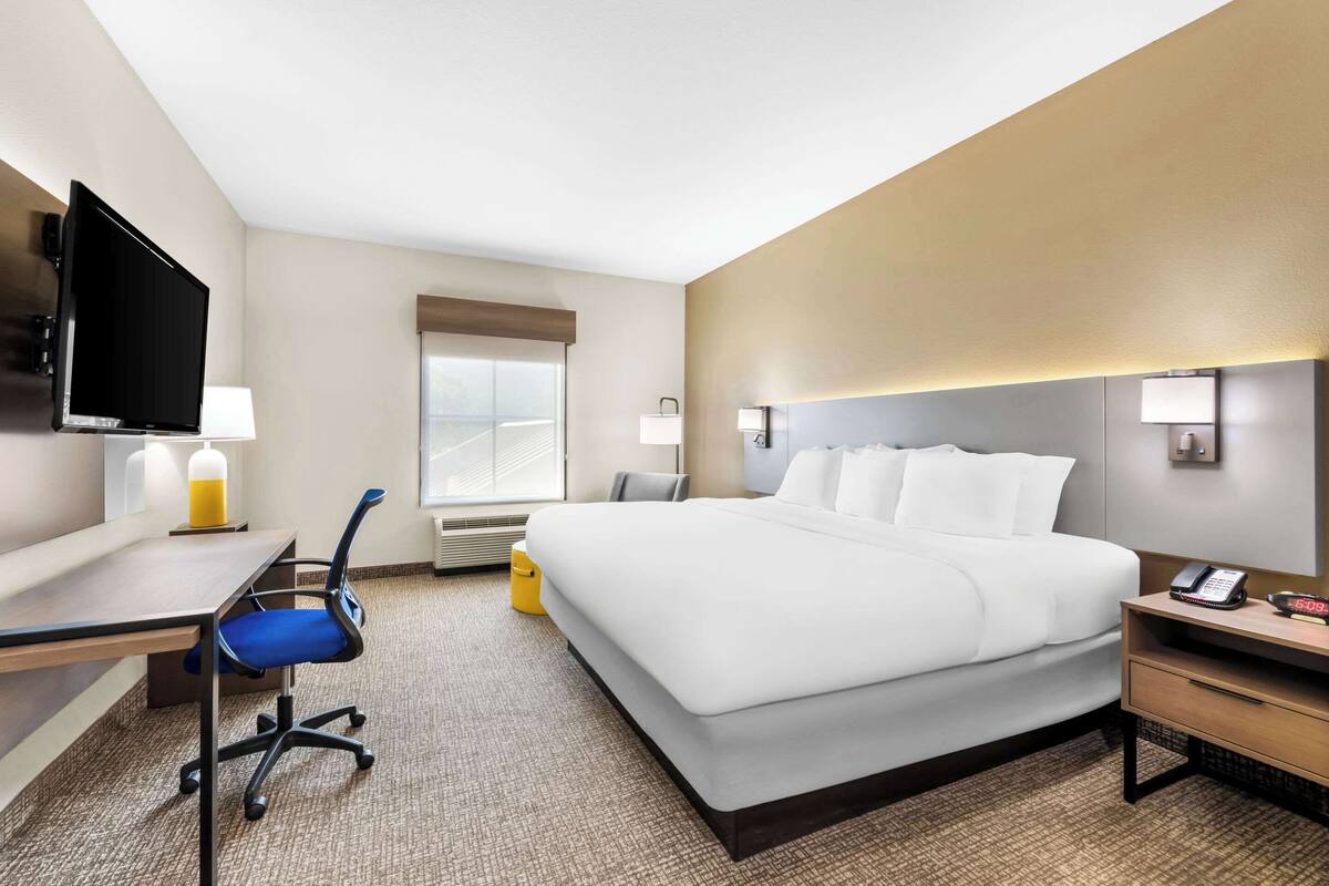 A hotel room with a bed, desk, chair, TV, bedside lamps, and a window.