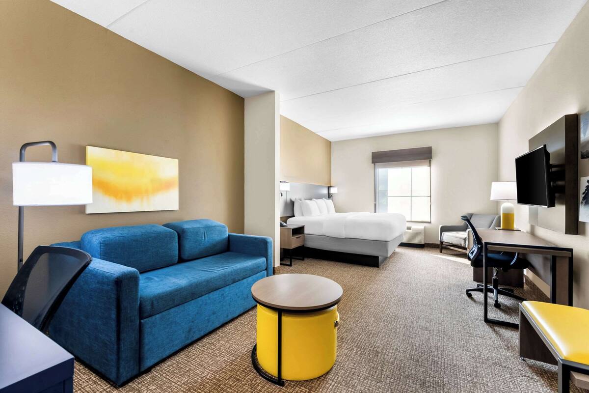 A hotel room with a blue sofa, a bed, a desk, a chair, and a small round table.