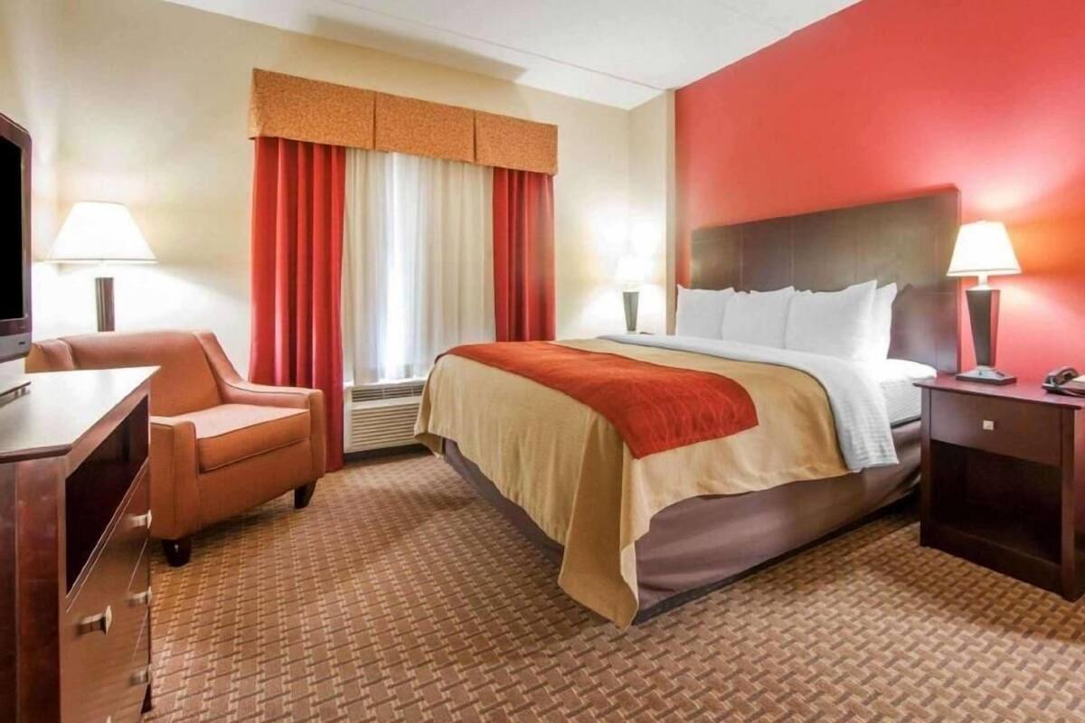 A hotel room with a bed, a desk, a chair, a TV, and a window with curtains.
