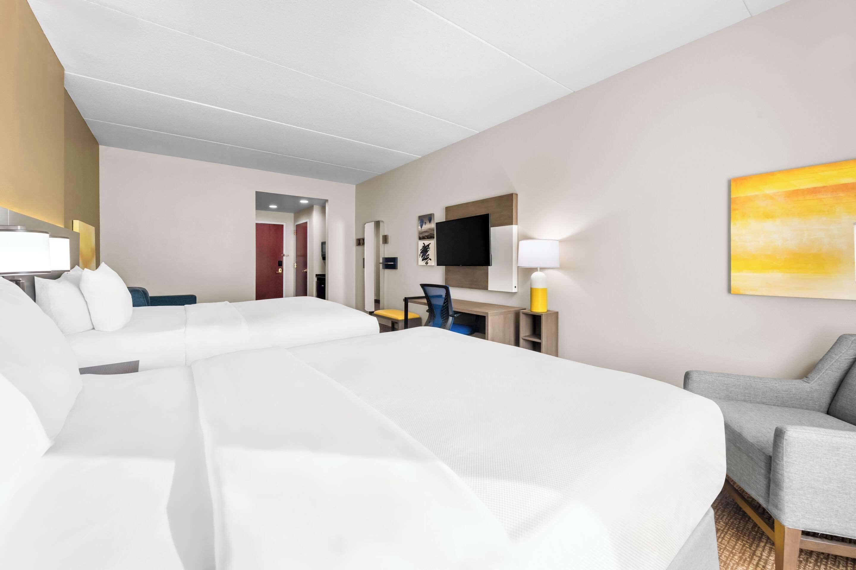 A hotel room with two large beds, a desk with a chair, a TV, and a painting on the wall.
