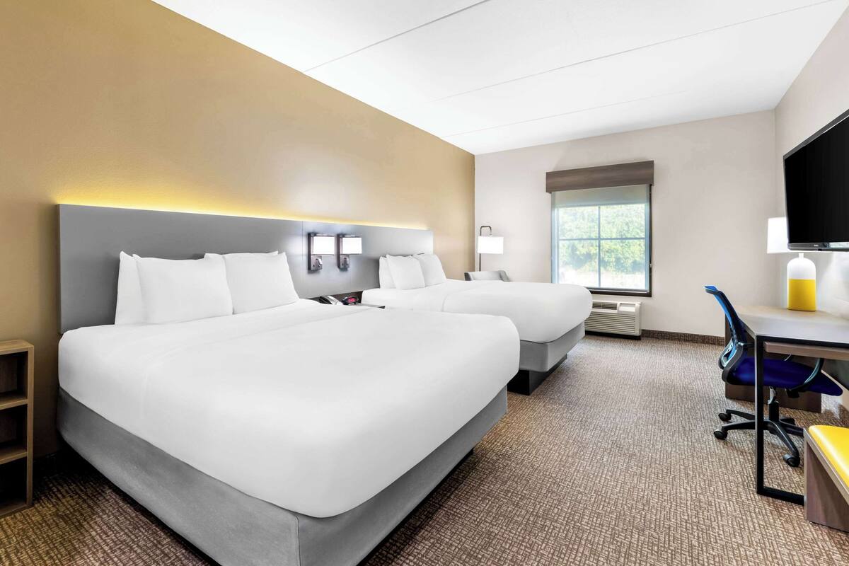 A hotel room with two beds, a desk, a chair, a TV, and a window.