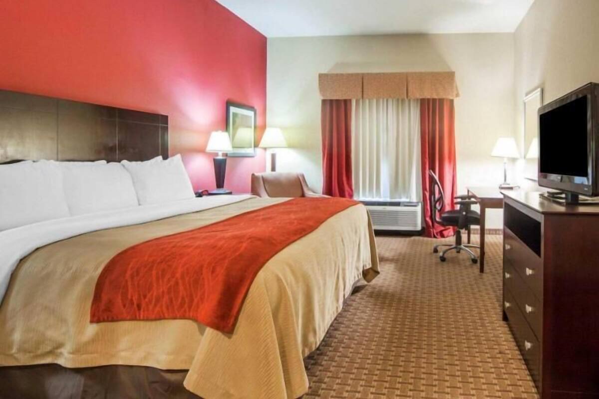 A hotel room with a large bed, a desk with a television, a chair, and a window with curtains.