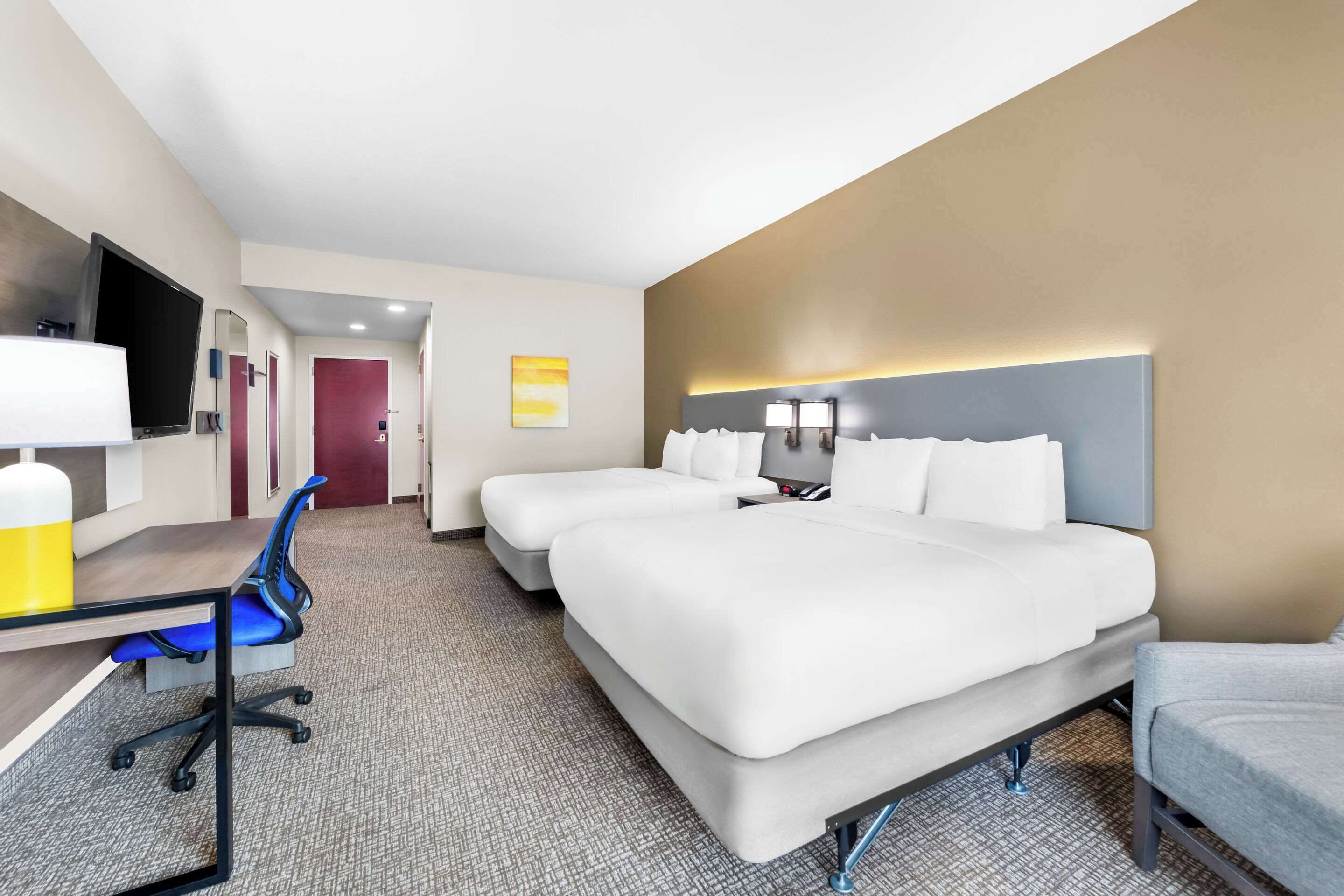 A hotel room with a large bed, a desk with a chair, a TV, and a bathroom door.