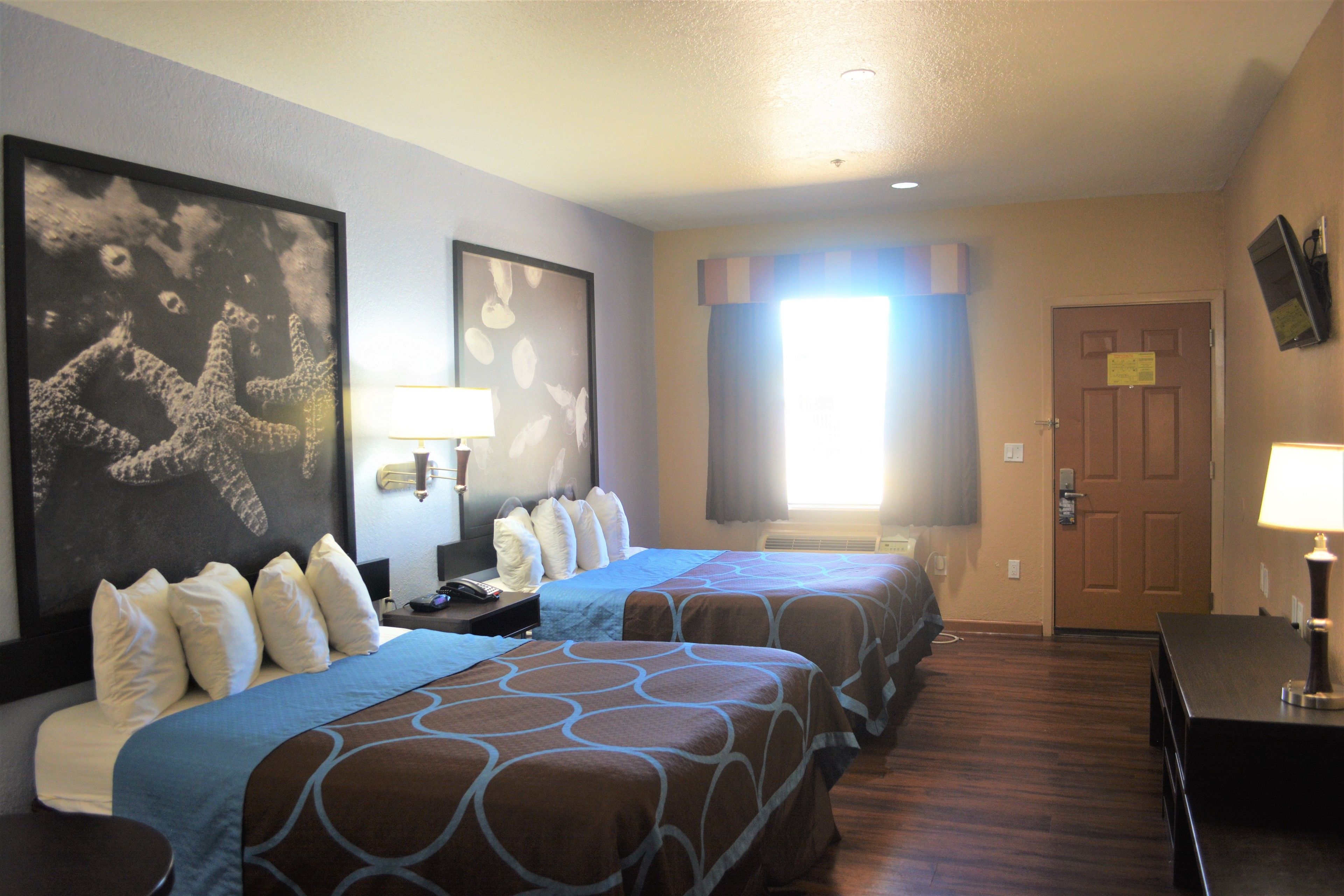 A hotel room with two beds, a desk, a chair, a TV, and artwork on the walls.