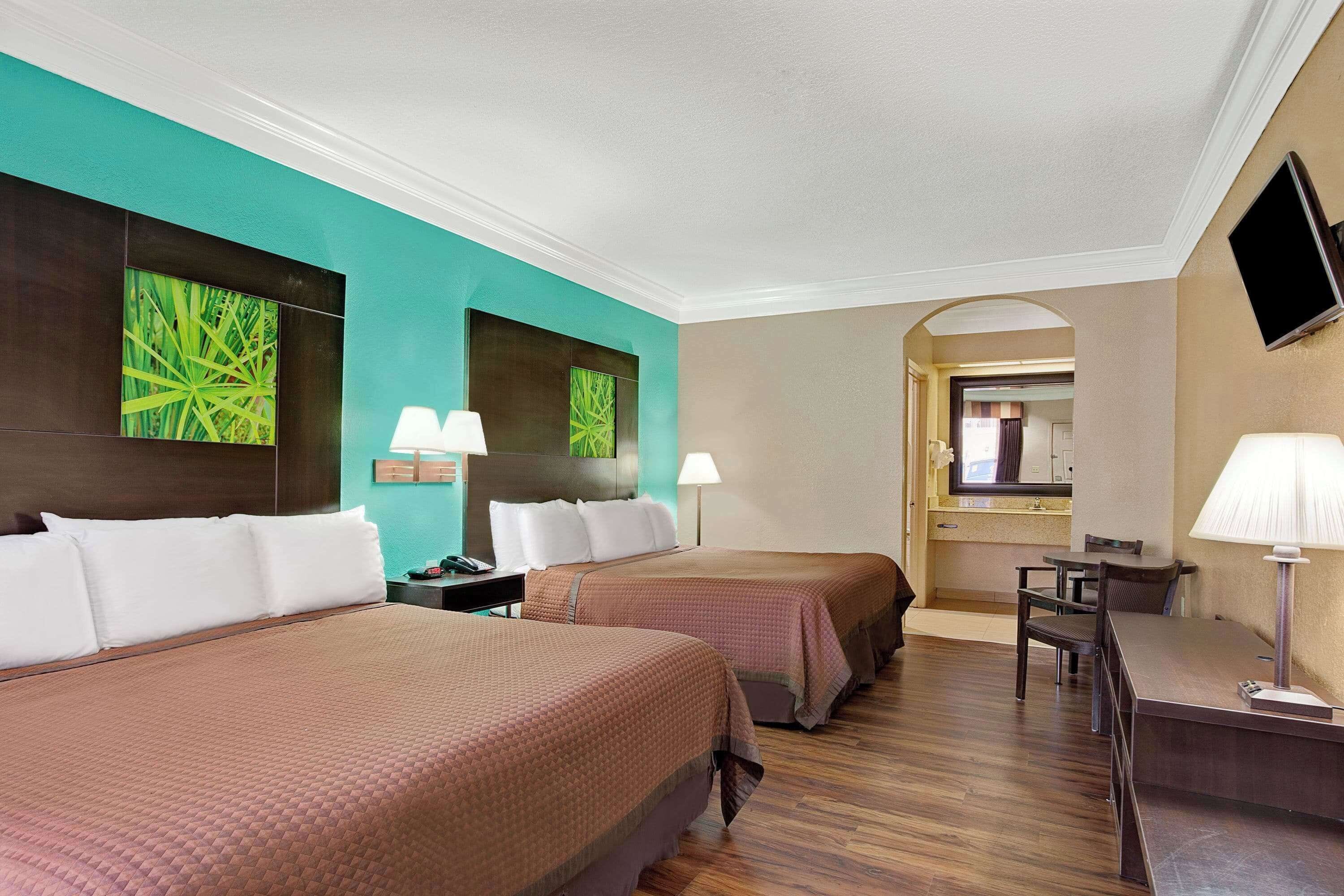 A hotel room with two beds, a desk, and a TV.