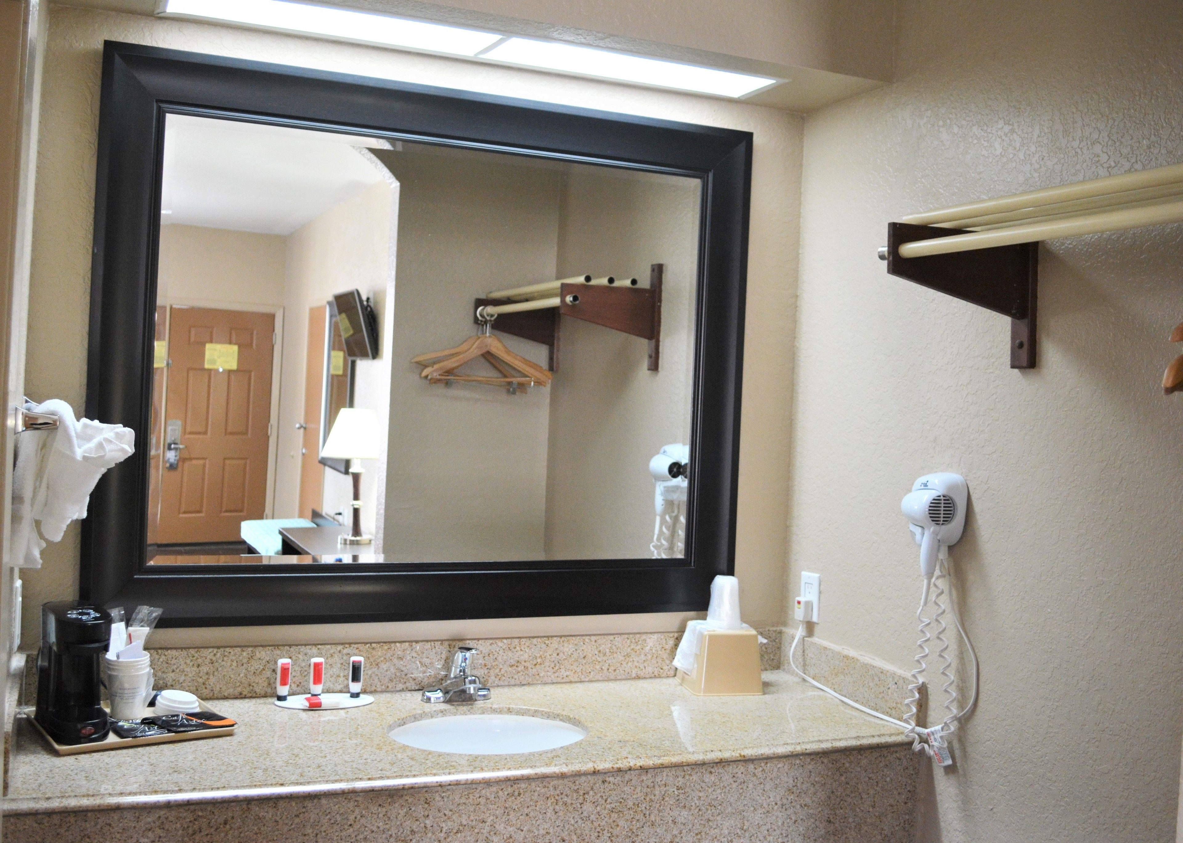 A hotel bathroom with a large mirror, sink, and towel rack.