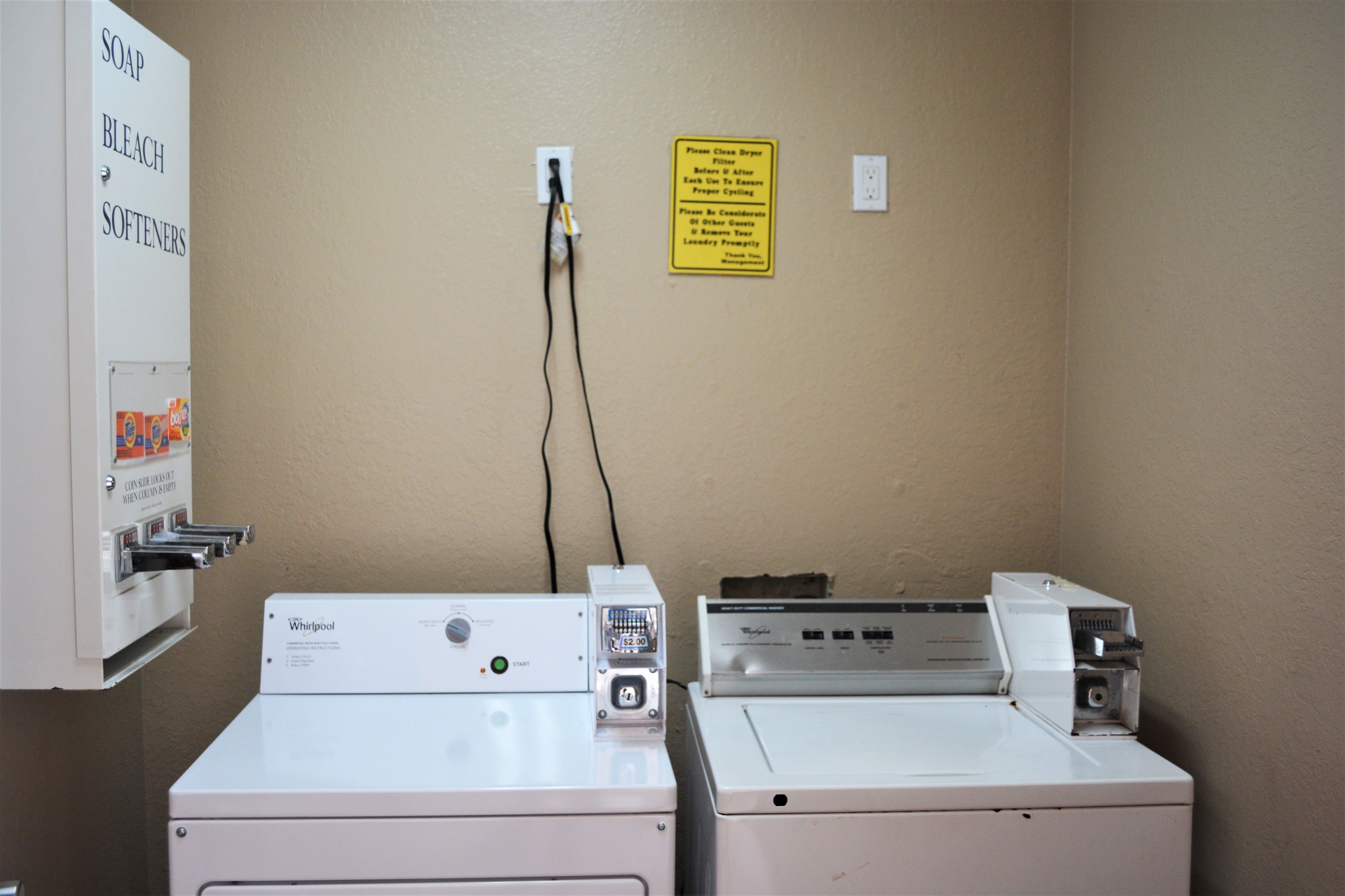 A laundry room with two Whirlpool washers and a dryer, a soap and bleach dispenser, and a sign with laundry instructions.