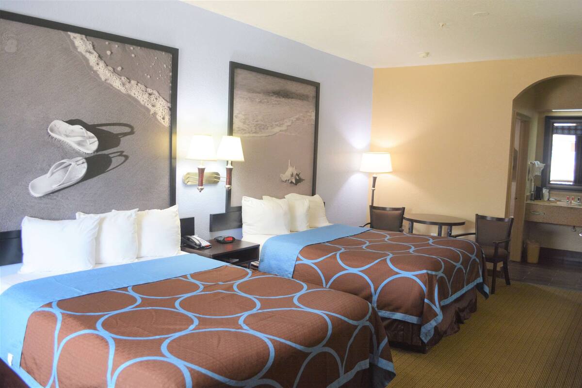 Ein Hotelzimmer mit zwei Betten, einem Schreibtisch und einem Stuhl. Auf dem Schreibtisch stehen zwei Lampen und darüber hängt ein Spiegel.