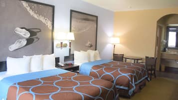 Quarto de hotel com duas camas, uma escrivaninha e uma cadeira. Há duas luminárias na escrivaninha e um espelho acima dela.
