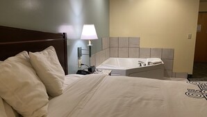 Ett hotellrum med en säng, ett nattduksbord med en lampa och ett badrum med badkar och handfat.