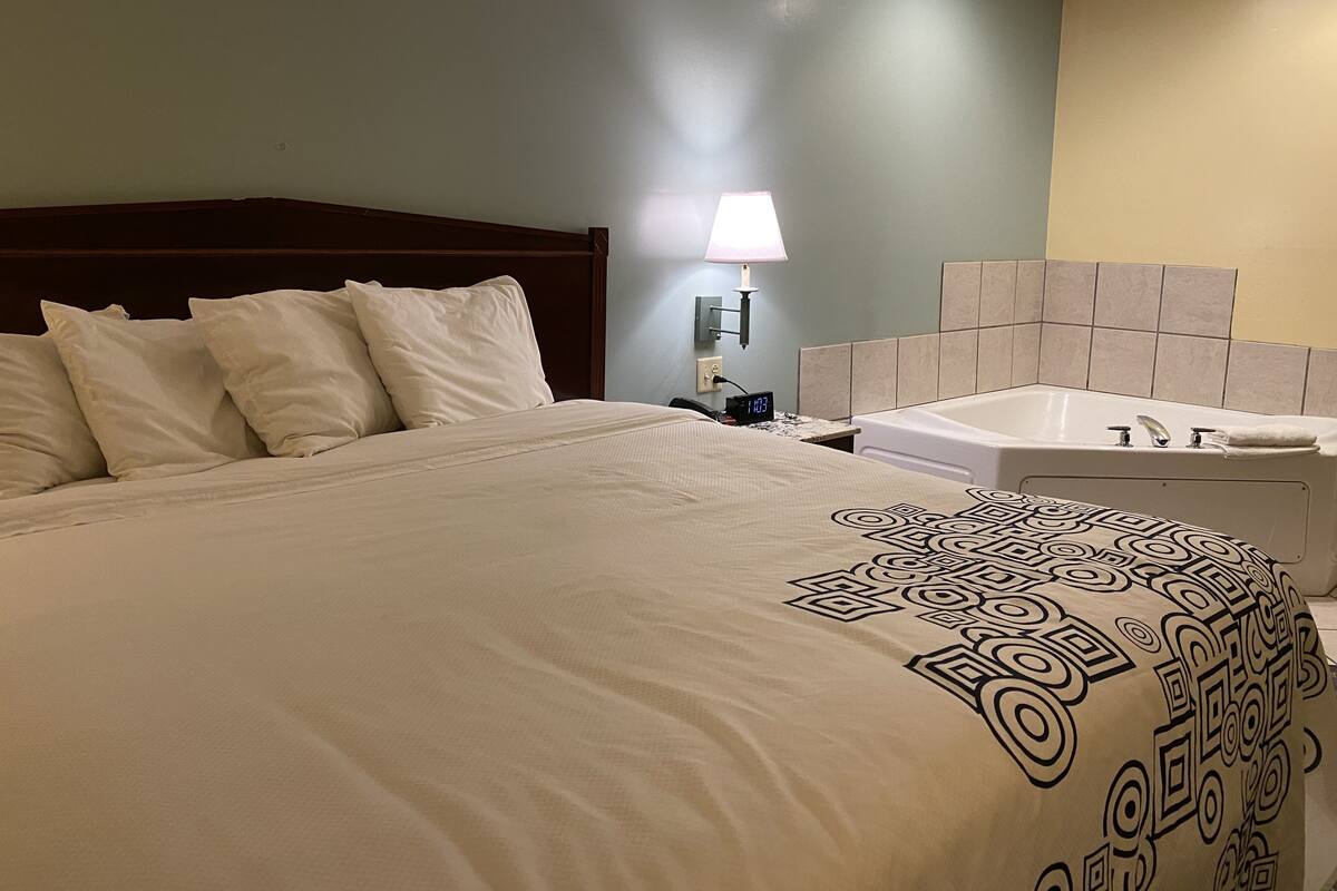 Quarto de hotel com uma cama grande, mesa de cabeceira com abajur e banheiro com banheira.