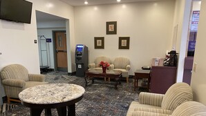 En hotellobby med randiga soffor, ett soffbord i marmor, inramade konstverk på väggen, en bankomat och en tv som är monterad på väggen.