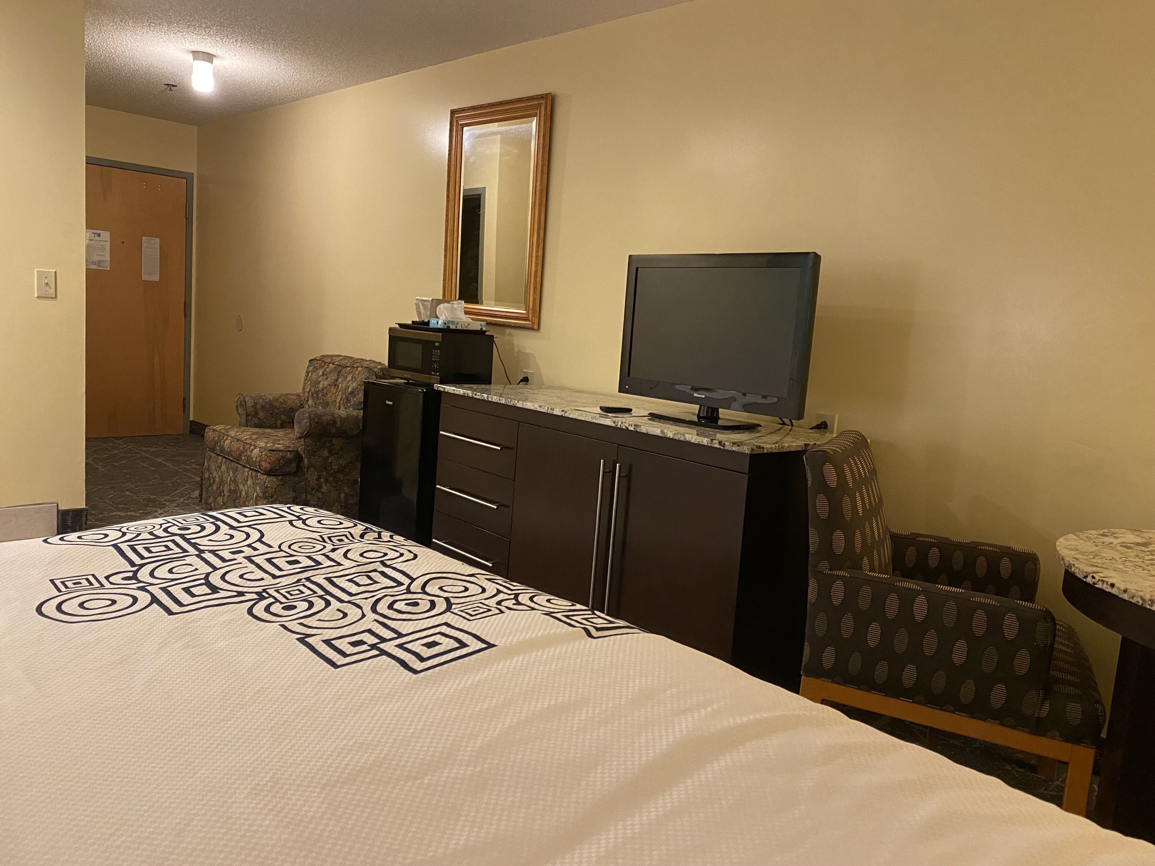 Une chambre d’hôtel équipée d’un lit, d’un bureau avec un ordinateur, d’une chaise, d’une petite table et d’un four à micro-ondes.