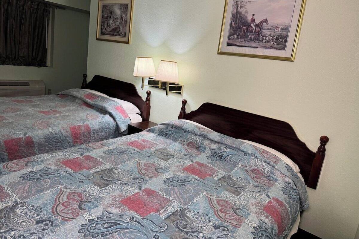 A hotel room with two beds, a nightstand with lamps, and two framed pictures on the wall.
