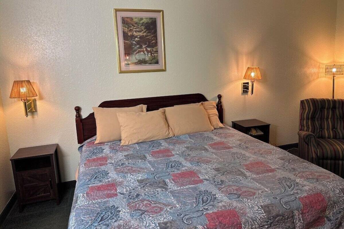A hotel room with a bed, two bedside lamps, a framed picture on the wall, and a striped armchair.