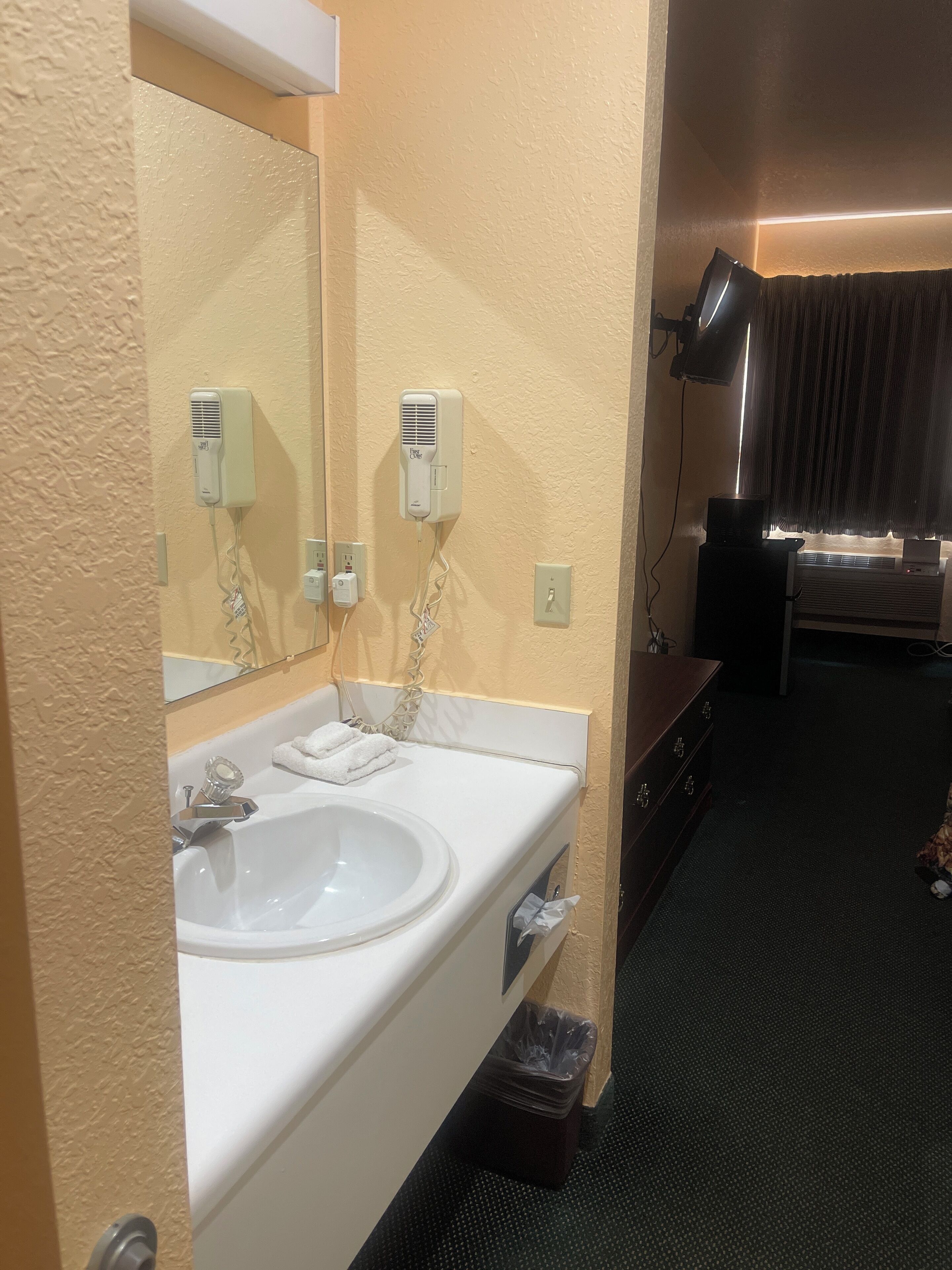A hotel bathroom with a sink, mirror, towel dispenser, and a trash bin.