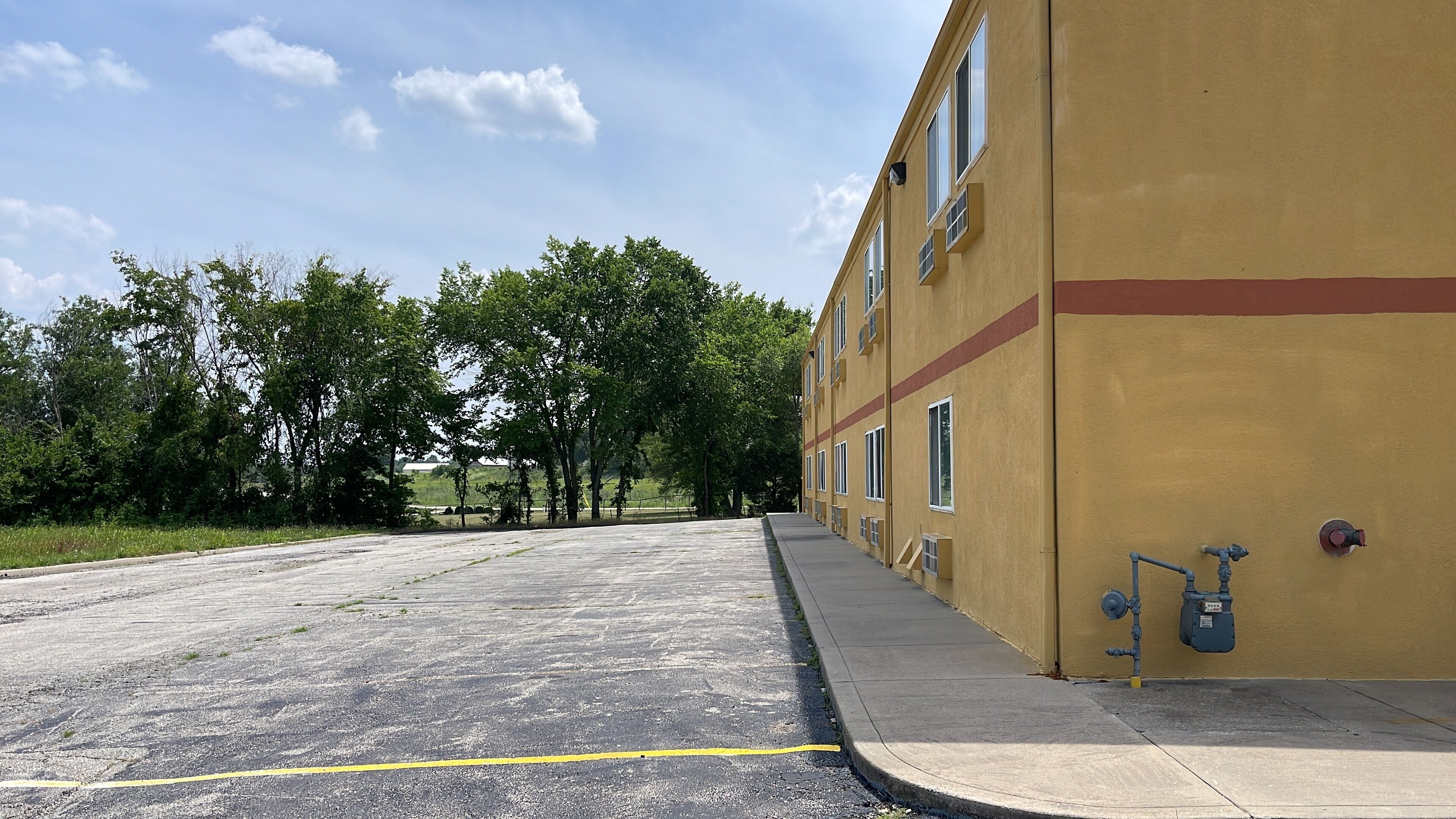 Un estacionamiento con un edificio amarillo, árboles y cielo despejado.