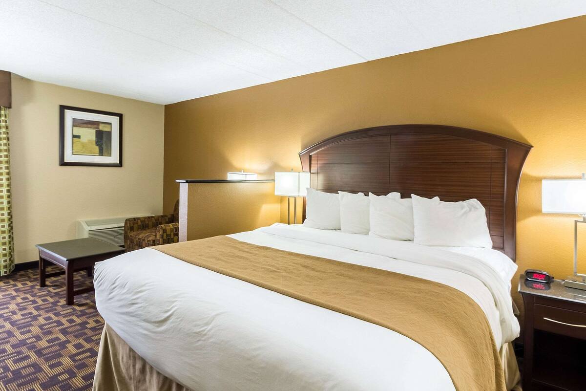 A hotel room with a large bed, two bedside tables, a chair, a desk, and a lamp.