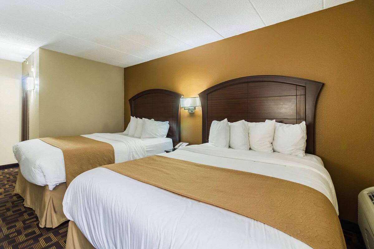 A hotel room with two beds, beige walls, and a patterned carpet.