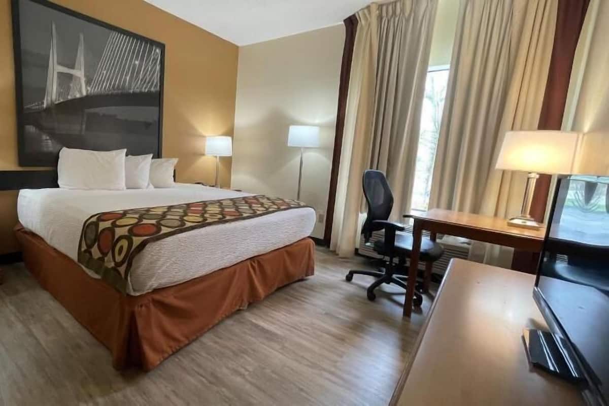 A hotel room with a bed, desk, chair, lamps, and a large wall art piece.