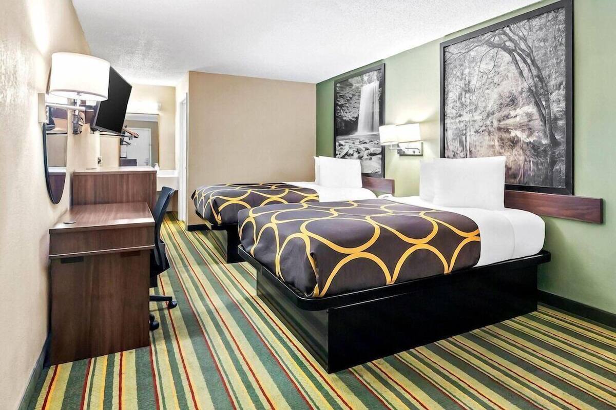 A hotel room with two beds, a desk, a chair, and a large window.