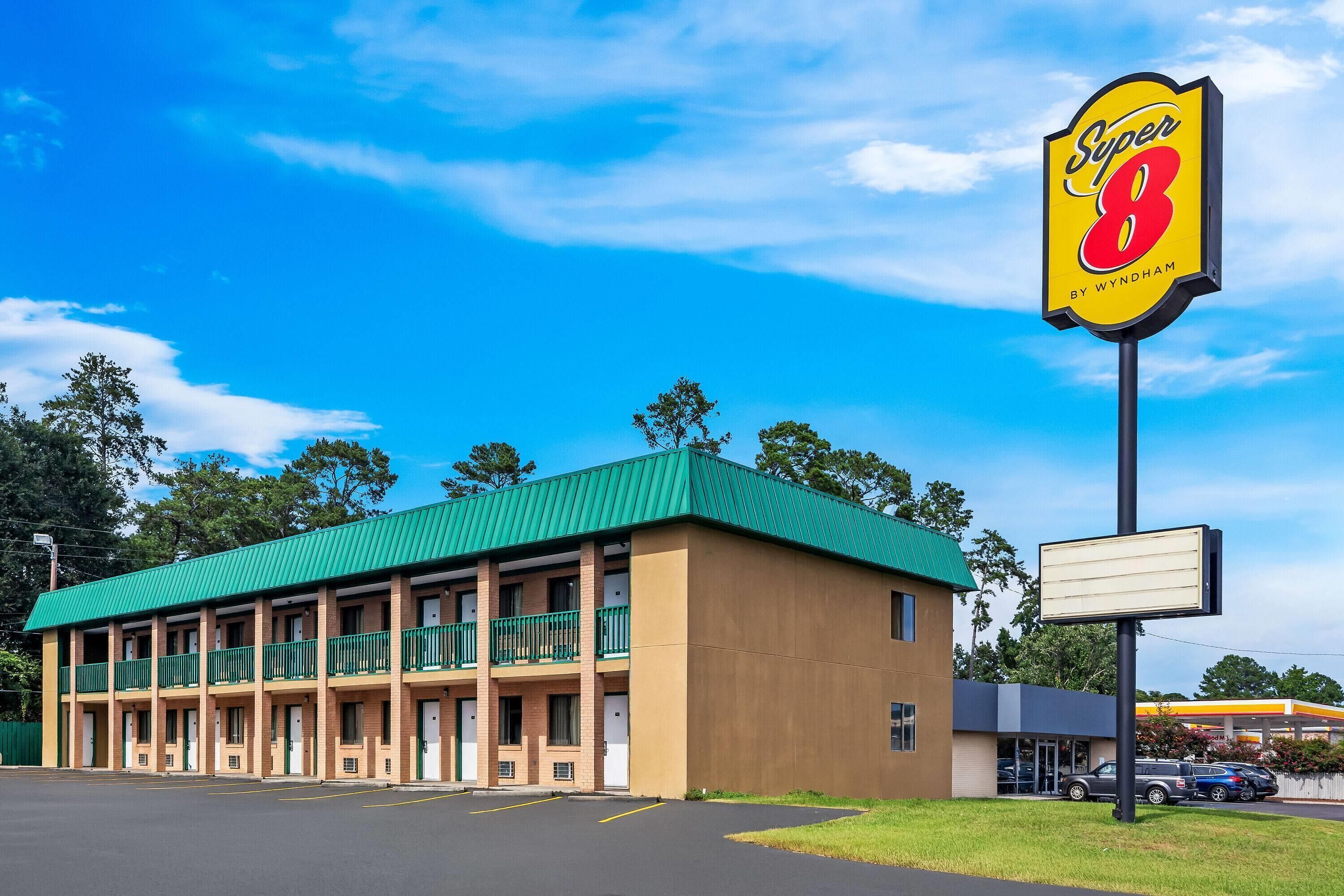 Un motel con tetto verde, diverse camere e un grande cartello Super 8 by Wyndham.