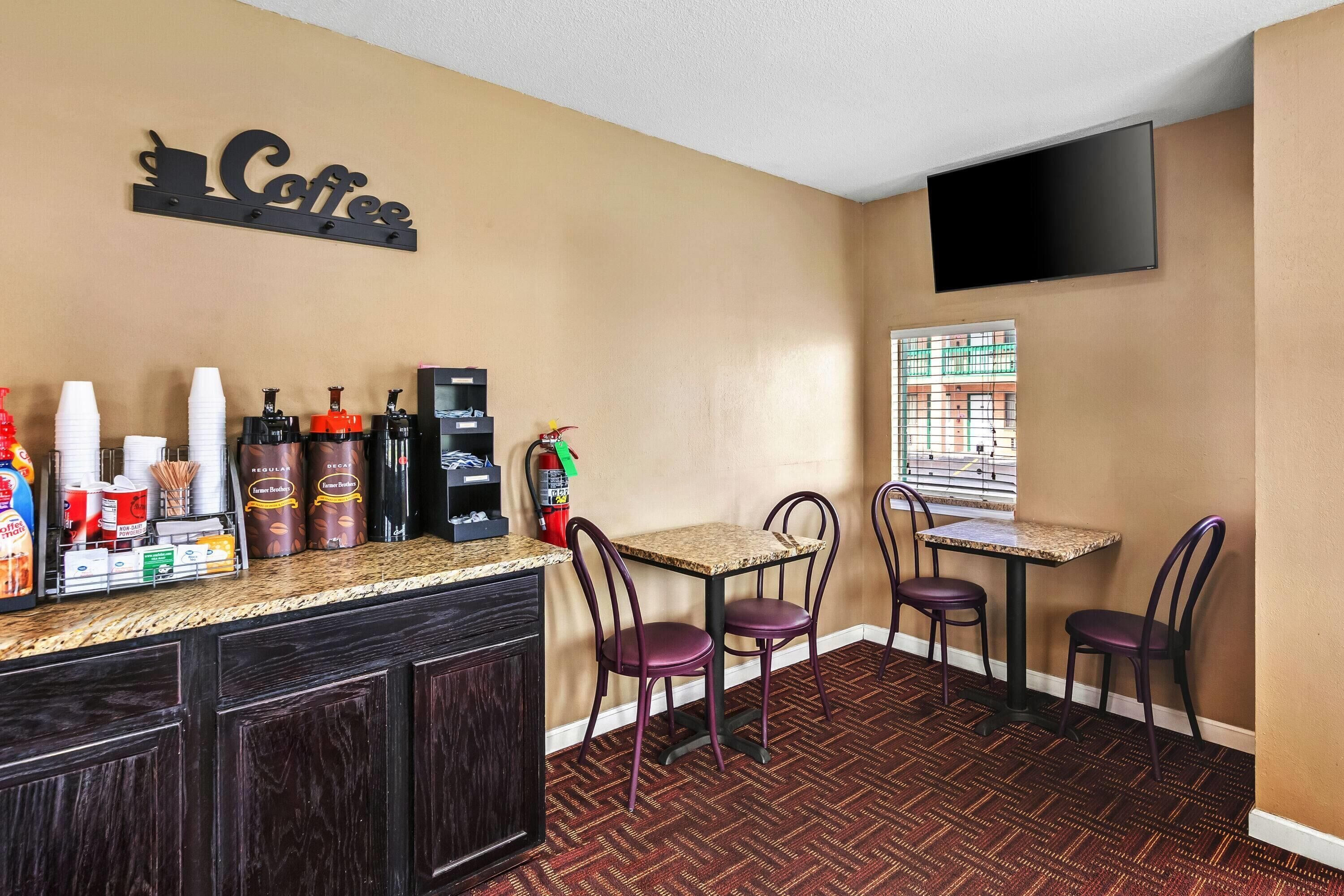 A coffee bar with a 'Coffee' sign, a TV mounted on the wall, and a window with a view of buildings.