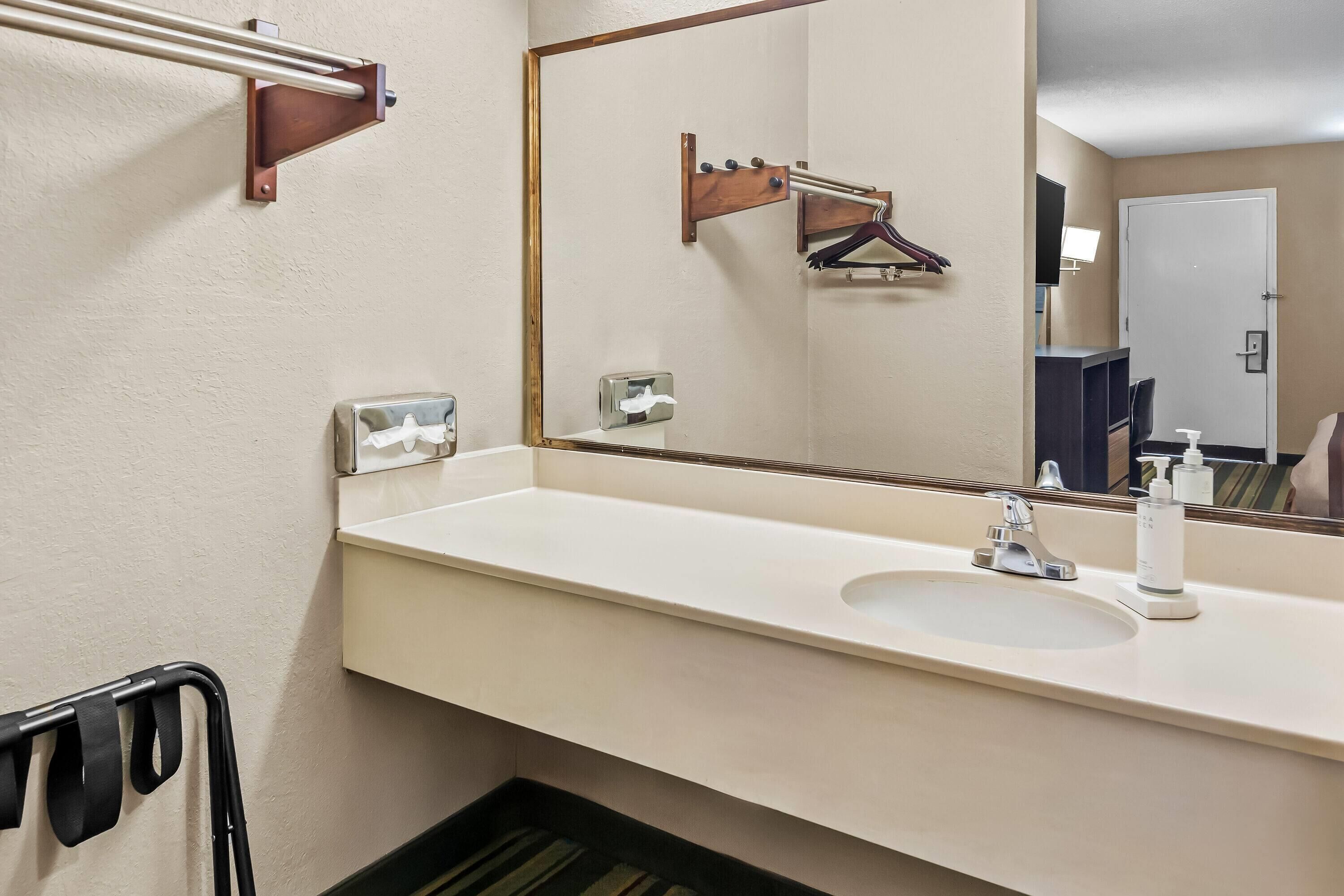A bathroom with a white sink, a mirror, and a towel dispenser.
