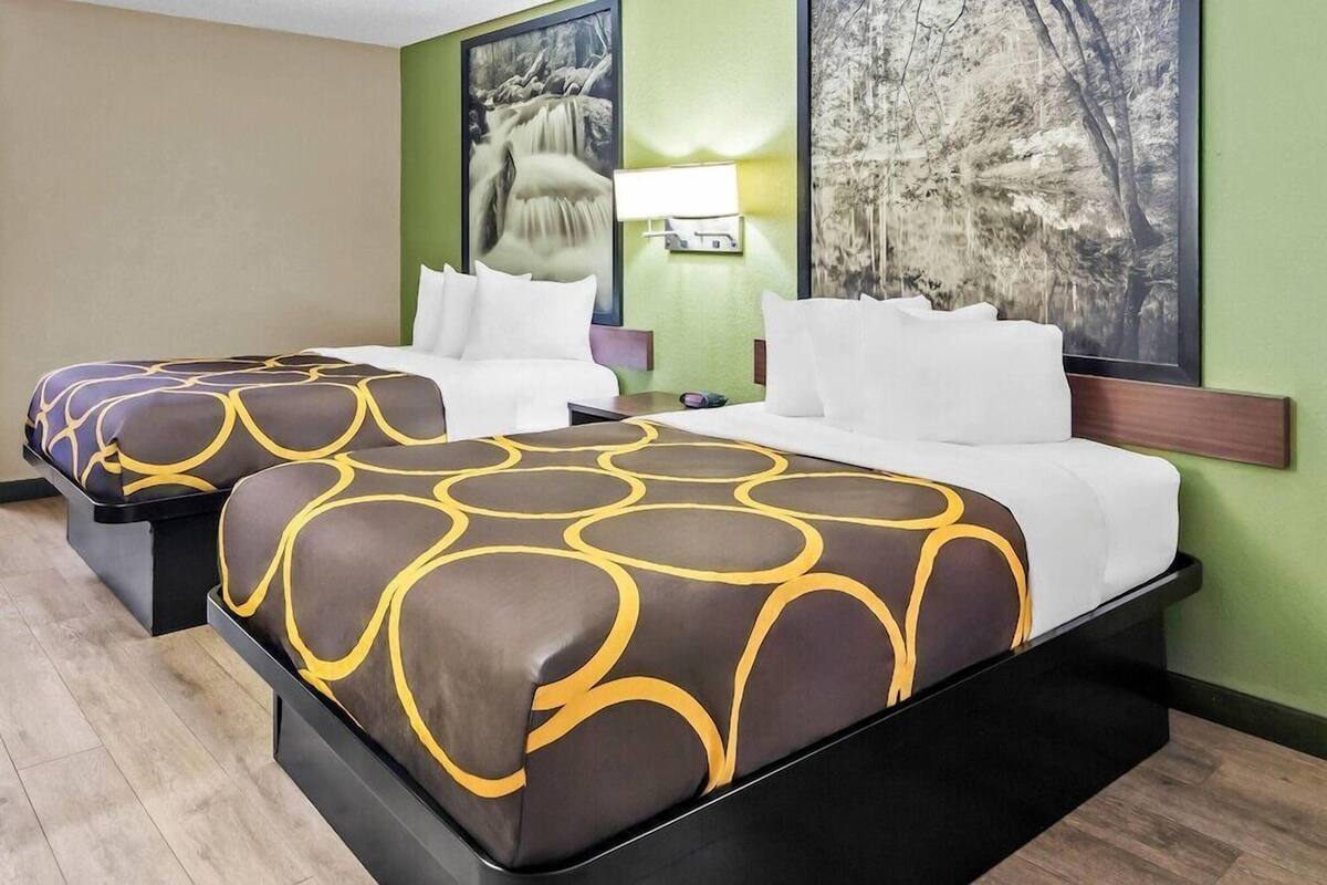 Two beds with patterned covers, a wall-mounted lamp, and two framed pictures.