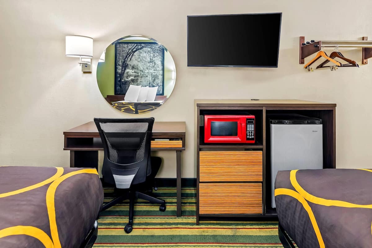 A hotel room with two beds, a desk with a chair, a microwave, a television, and a mirror.