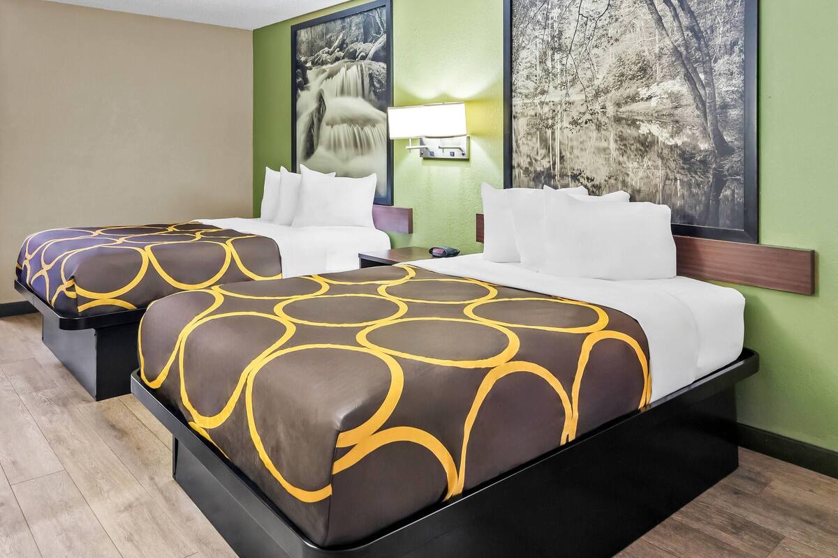 A hotel room with two beds, each with a patterned bedspread and white pillows.