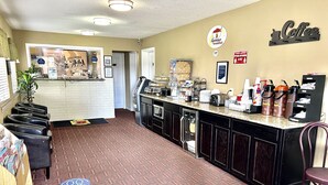 Un vestíbulo de hotel con mostrador de recepción, estación de café y alfombra estampada.