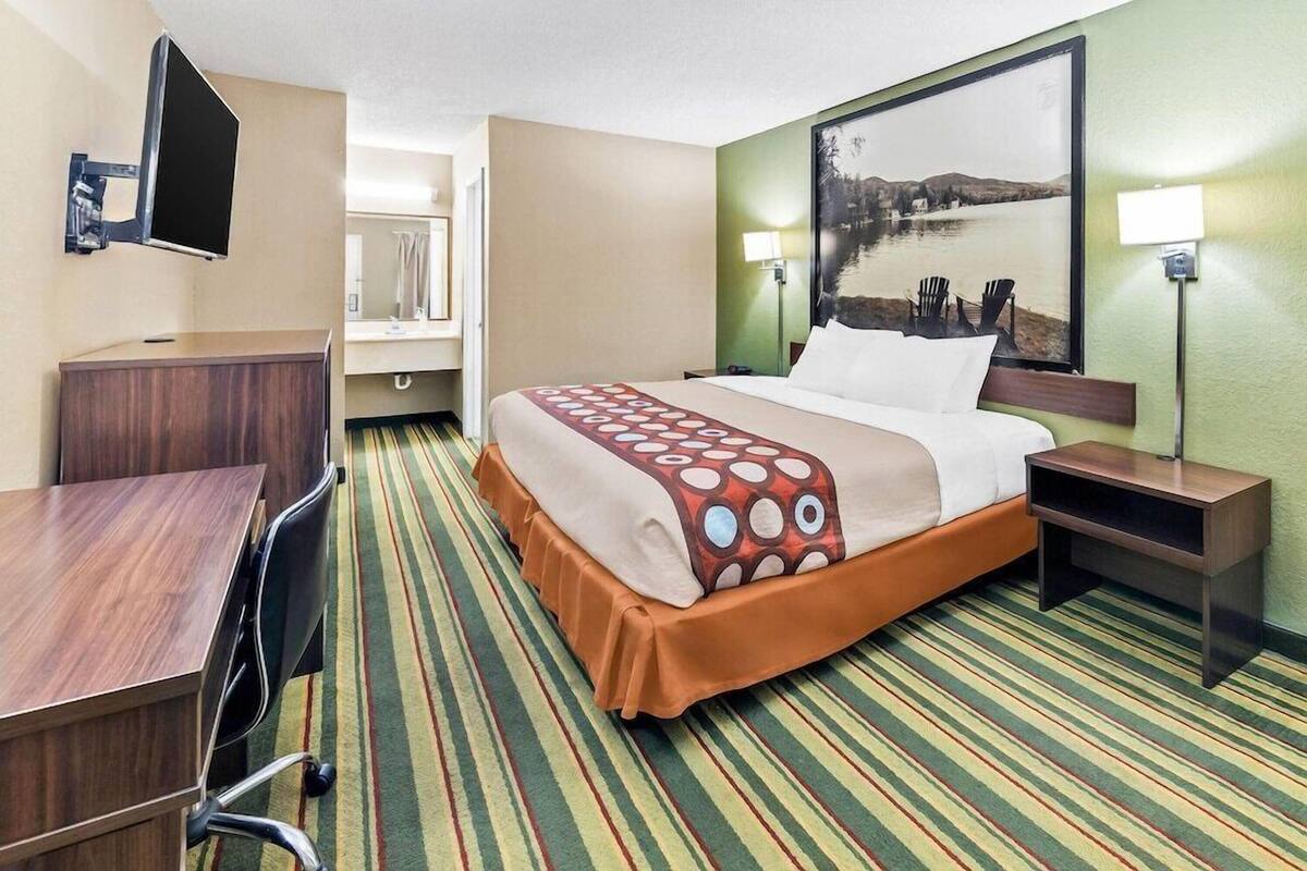 A hotel room with a bed, a desk, a chair, a TV mounted on the wall, and a painting on the wall.