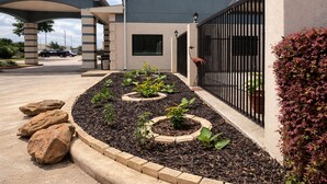 Un jardin aménagé avec des plates-bandes surélevées, un chemin pavé et un bâtiment doté d’une entrée fermée par un portail.