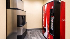 Une petite cuisine équipée d’une machine à café et d’un réfrigérateur contenant des boissons Coca-Cola.