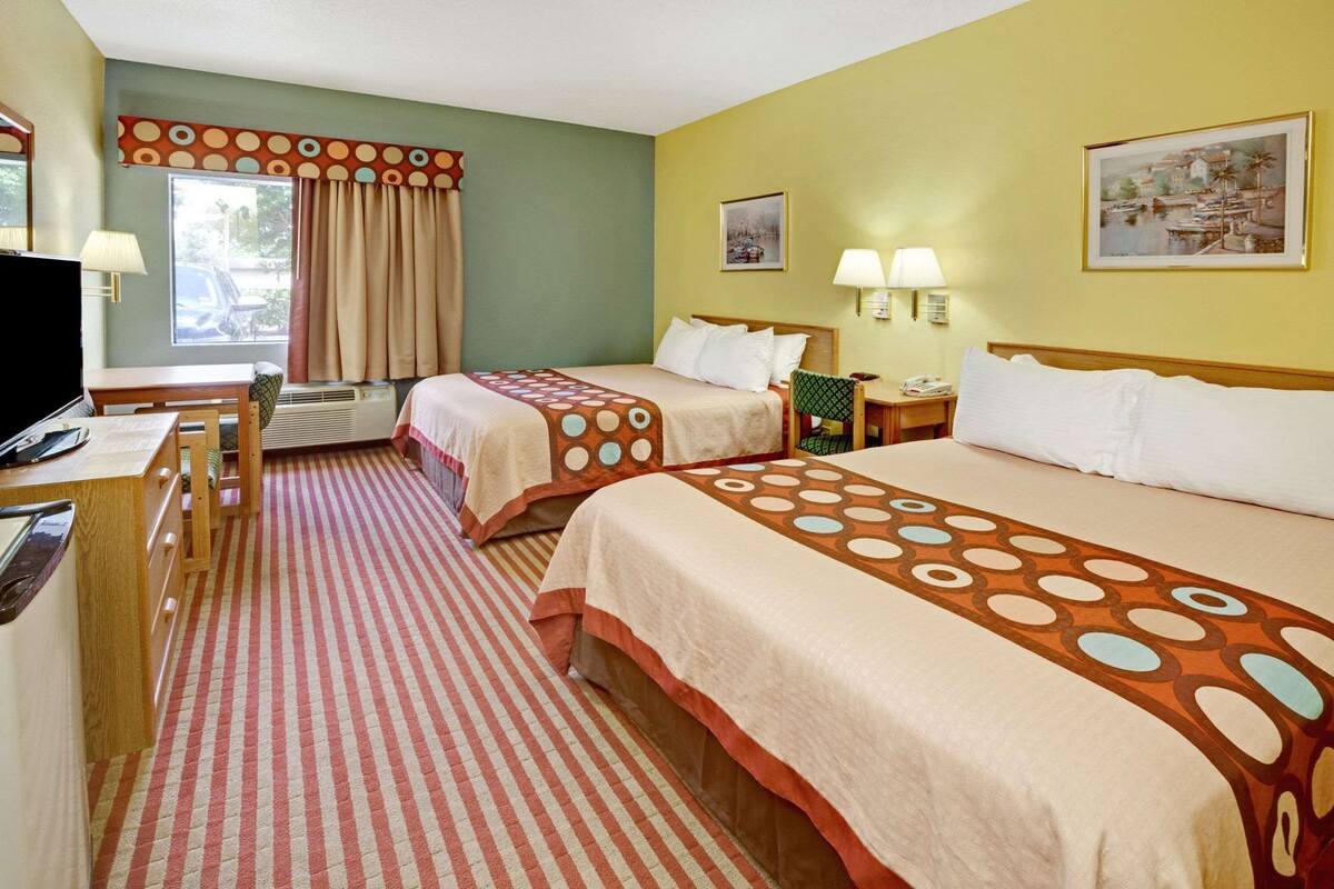 Quarto de hotel com duas camas, uma escrivaninha, uma cadeira e uma televisão.