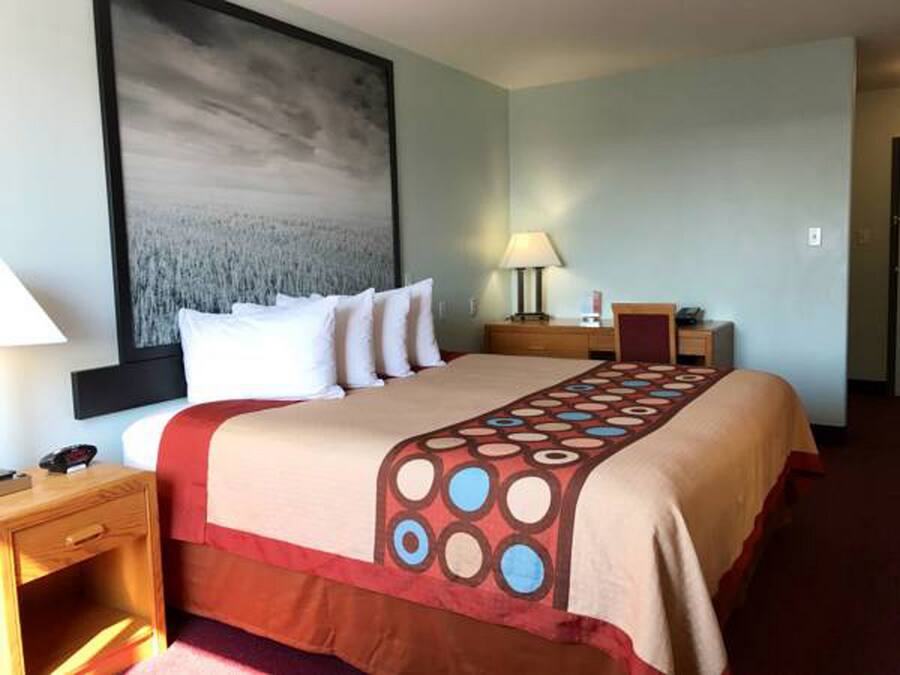 Habitación de hotel con cama, mesita de noche, escritorio, lámpara y un cuadro abstracto grande en la pared.