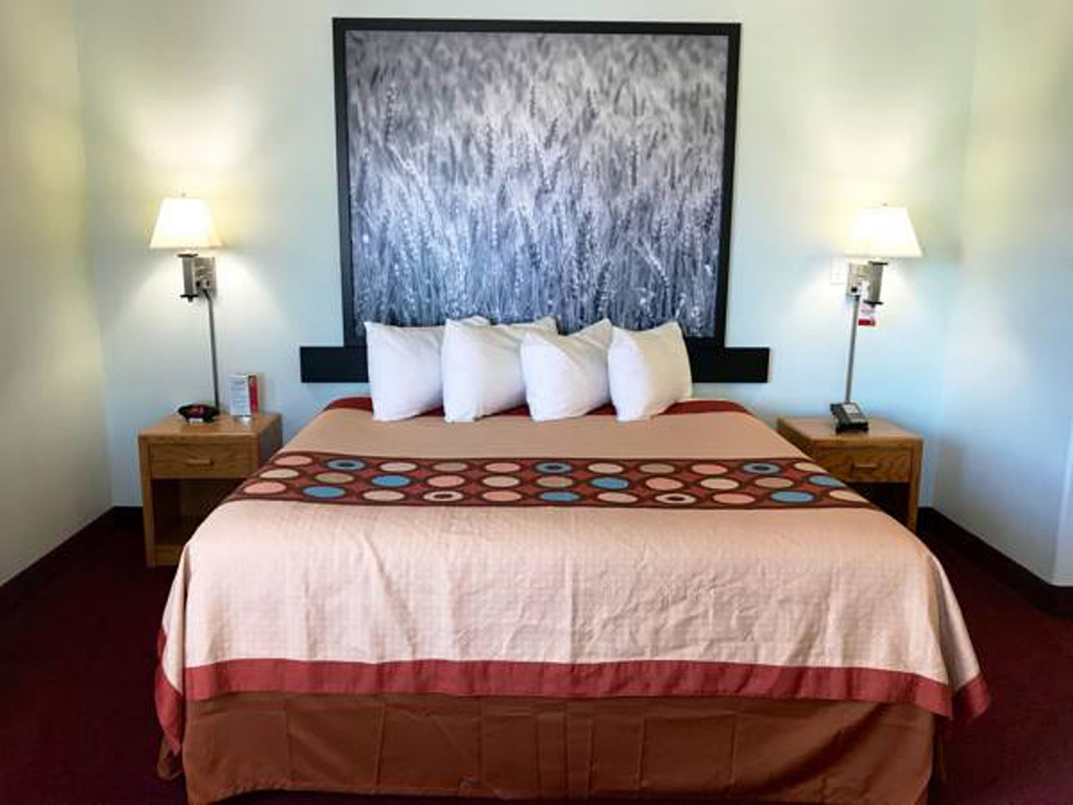 A hotel room with a large bed, two bedside tables, a nightstand, and a large abstract painting on the wall.