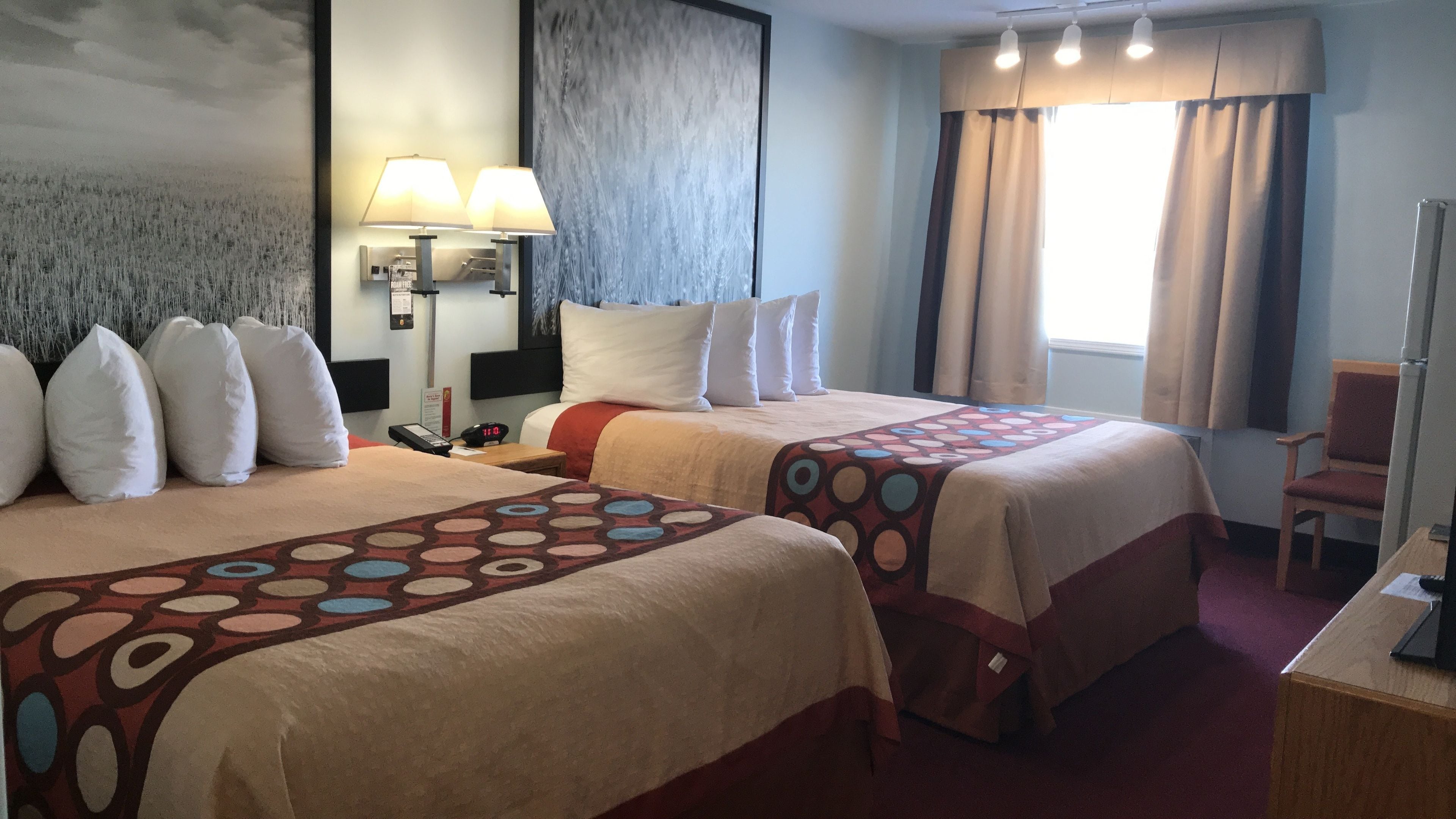 Ein Hotelzimmer mit zwei Betten, einem Nachttisch mit Lampe, einem Sessel und einem Schreibtisch.