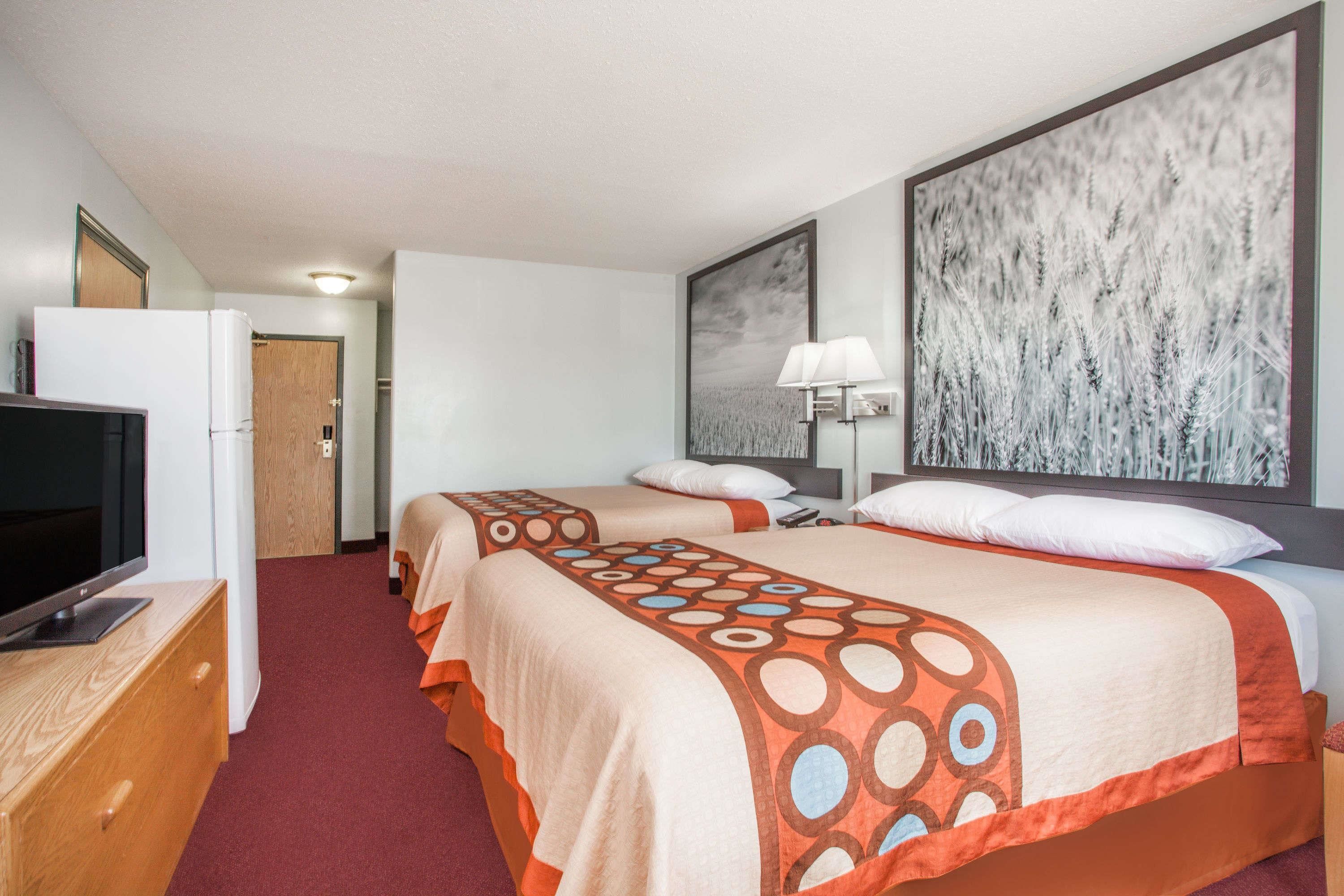 A hotel room with two beds, a TV, a desk, and a painting on the wall.