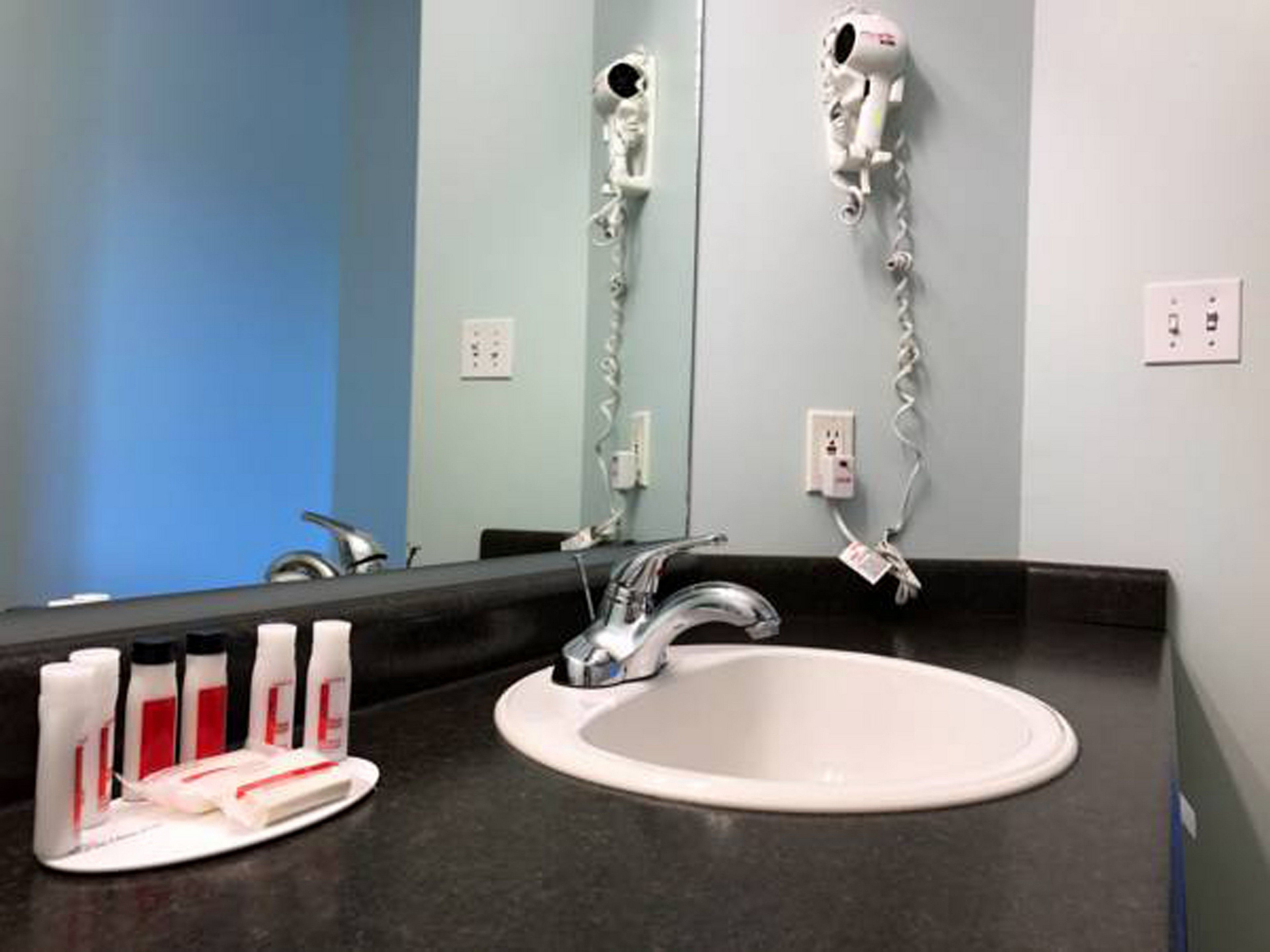 A bathroom with a white sink, a mirror, and a hairdryer mounted on the wall.