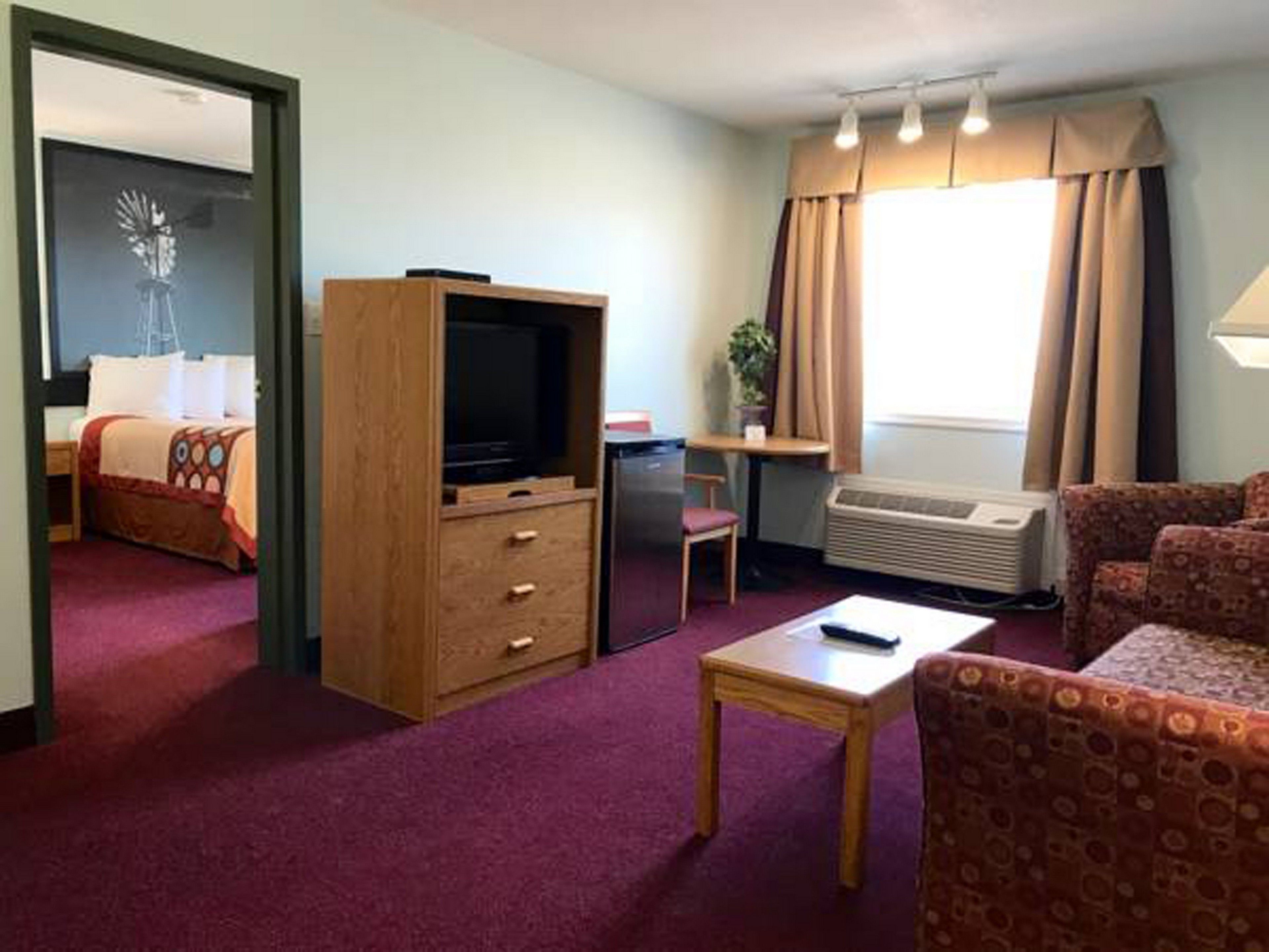A hotel room with a bed, a TV, a desk, a chair, a sofa, and a window with curtains.