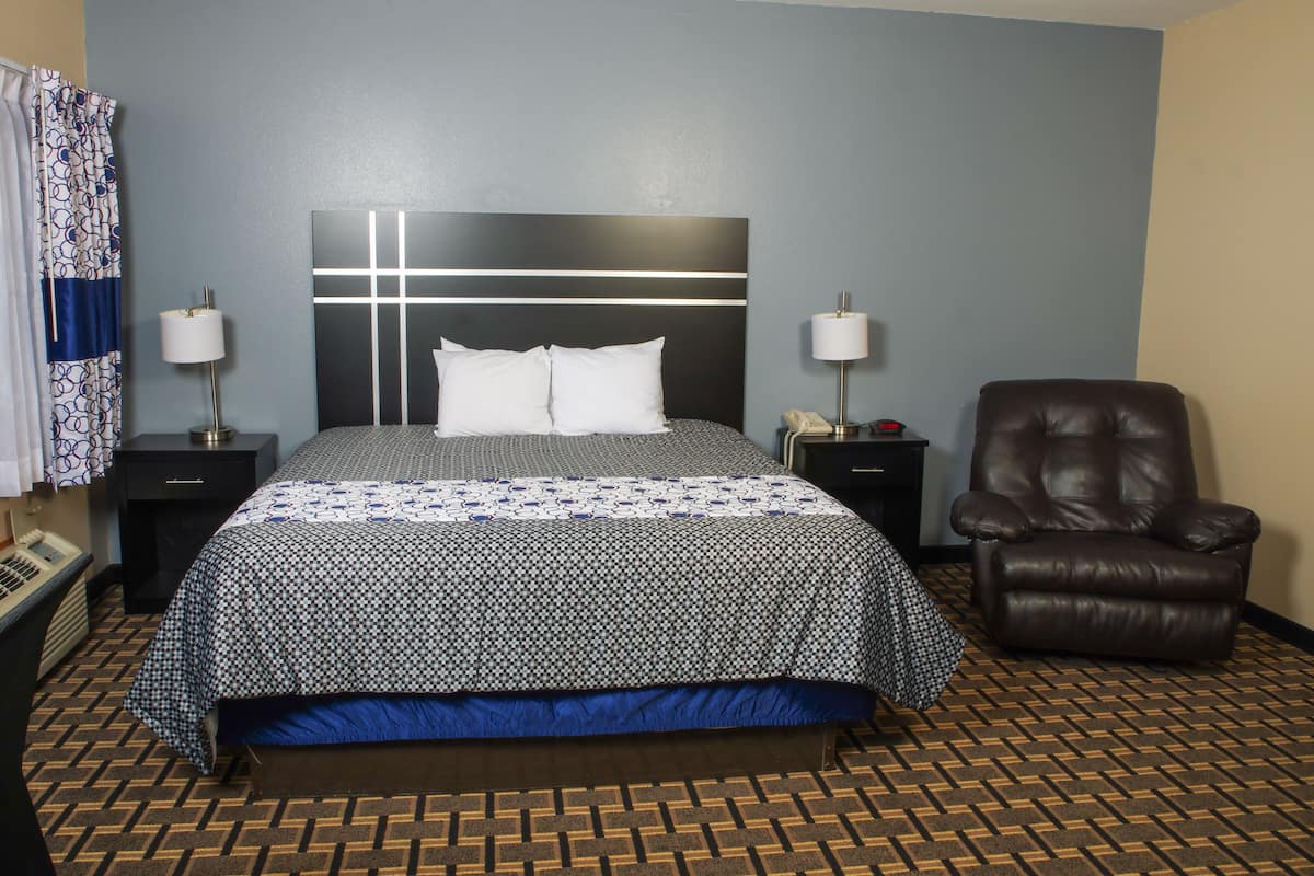 A hotel room with a large bed, two bedside tables with lamps, a leather armchair, and a patterned floor.